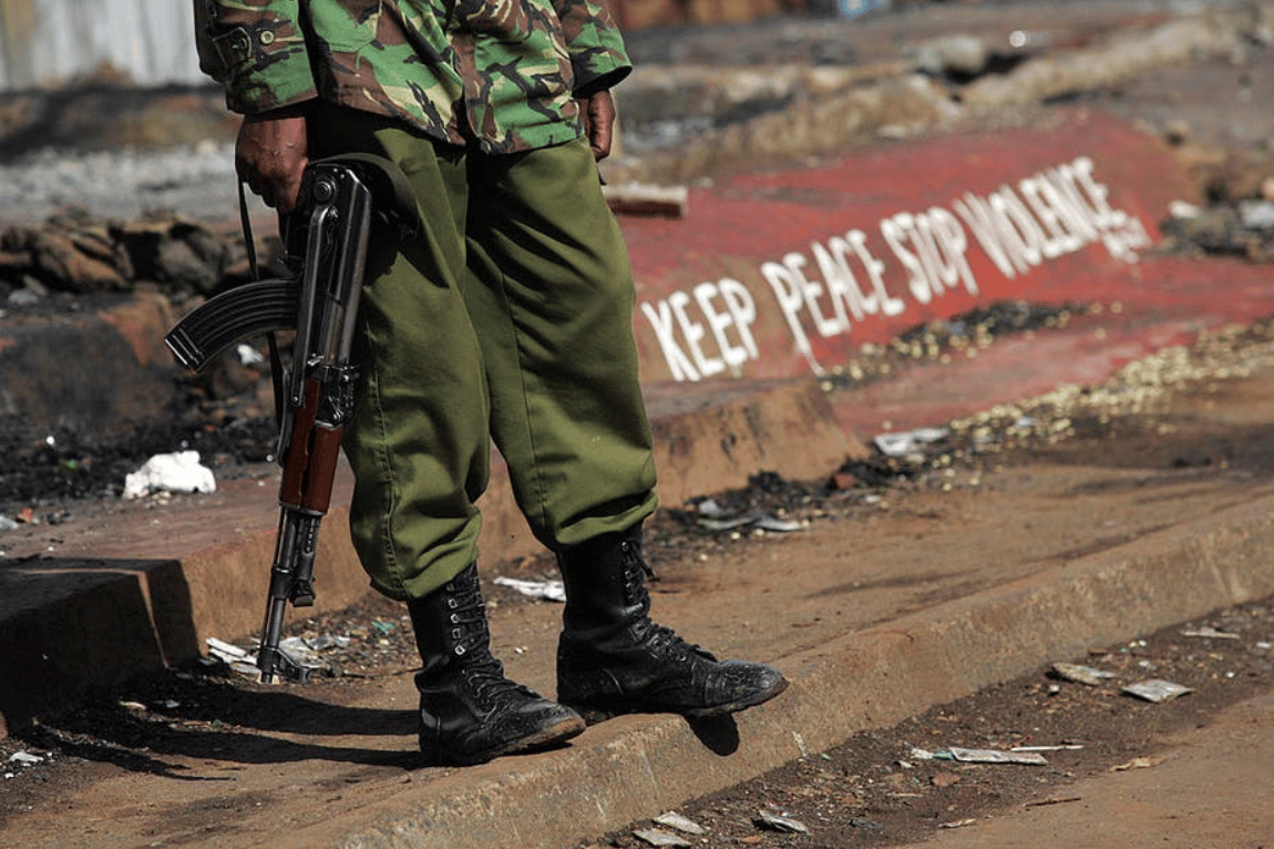 A Kenyan policeman stands next to a painted sign reading “keep peace stop violence” during protests in Nairobi in 2008 | AFP Roberto Schmidt