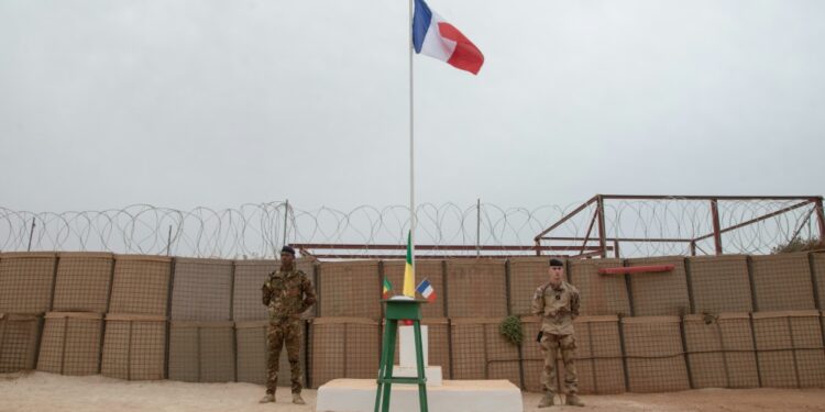 A Malian and a French soldier stand either side of a flagpole at a French base in Timbuktu before a ceremony last December to hand the facility over to the Malian military. Since then, France has announced a full pullout from Mali | AFP