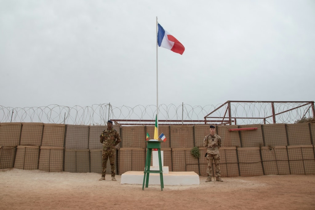 A Malian and a French soldier stand either side of a flagpole at a French base in Timbuktu before a ceremony last December to hand the facility over to the Malian military. Since then, France has announced a full pullout from Mali | AFP