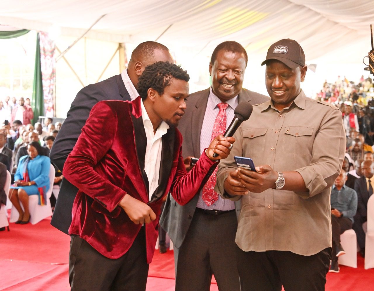President William Ruto registering for the Hustler Fund on November 30, 2022, as Prime Cabinet Secretary Musalia Mudavadi and Vincent Mutua (Chipukeezy) look on. PCS.