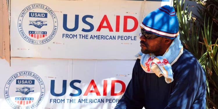 A refugee waits near boxes of USAID